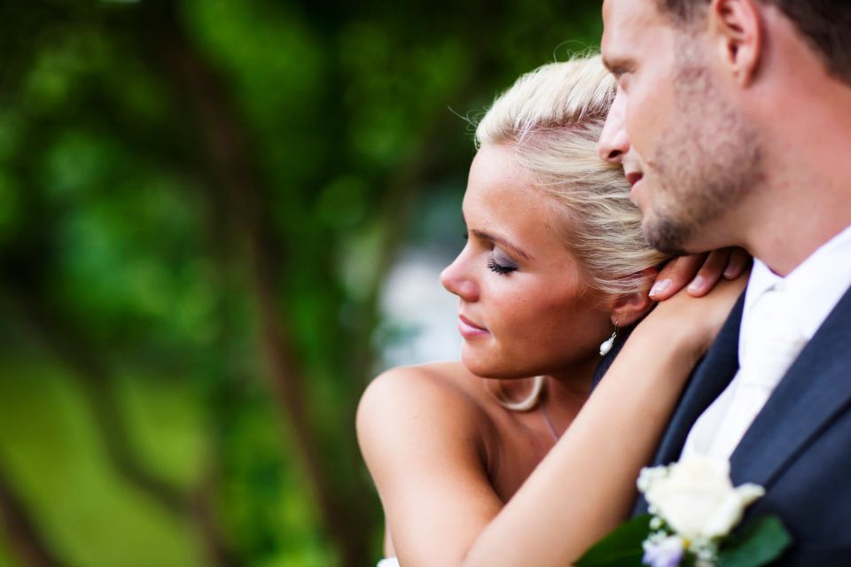 Bryllupsbillede i sort-hvid af nygift par. Kærlig brud læner sig ind mod sin brudgom i et ømt omfavnelsesøjeblik.