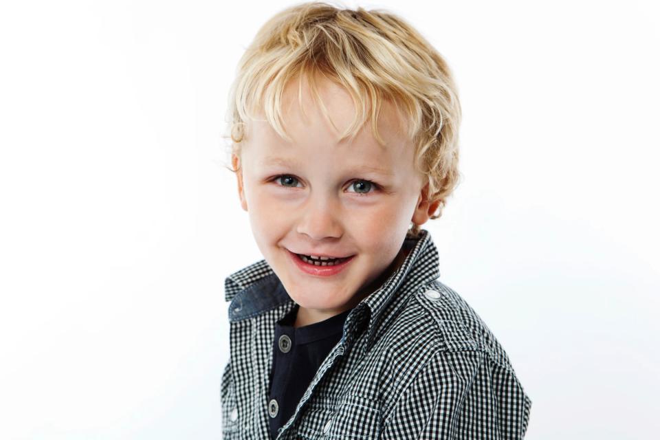 Glad barn med et autentisk smil. Dreng med lyst krøllet hår smiler varmt i blødt fotolys. Børn fotografering.