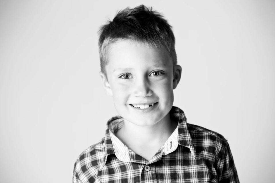 Sort/hvid portrætfoto af en smilende dreng i ternet skjorte, med tænder blottede og levende øjne.