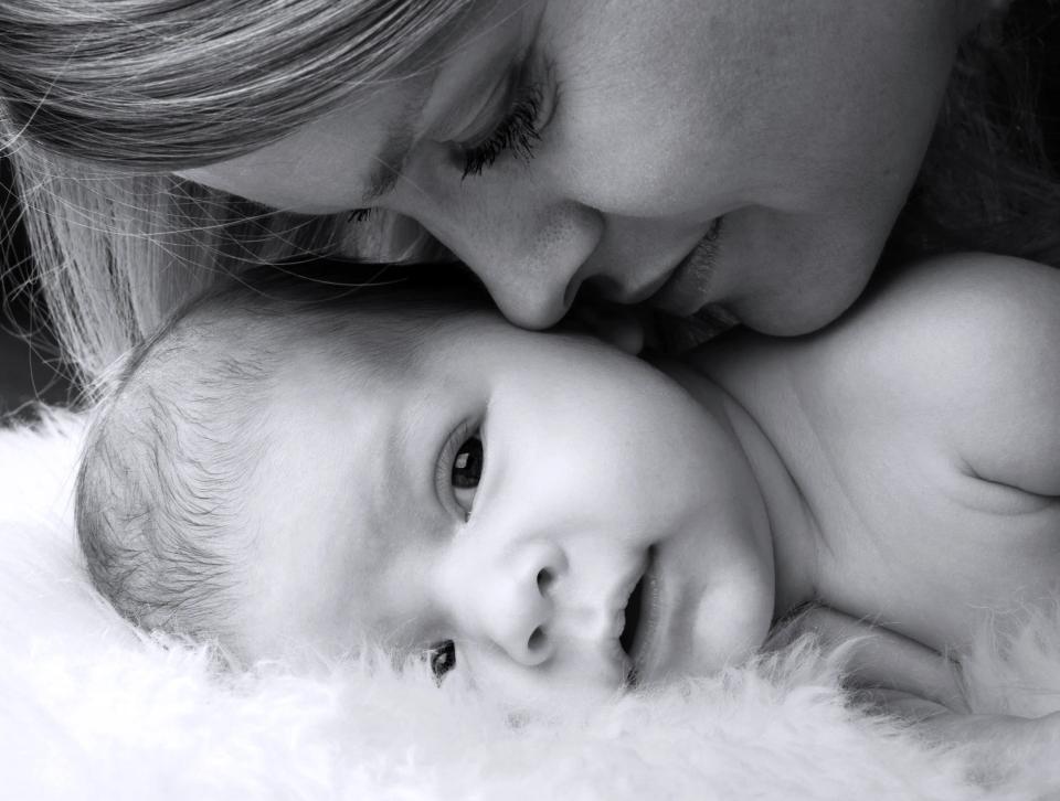 Sort/hvid babyfotografering af en mor, der ømt kysser sin baby på panden. Nærkontakt og kærlighed.