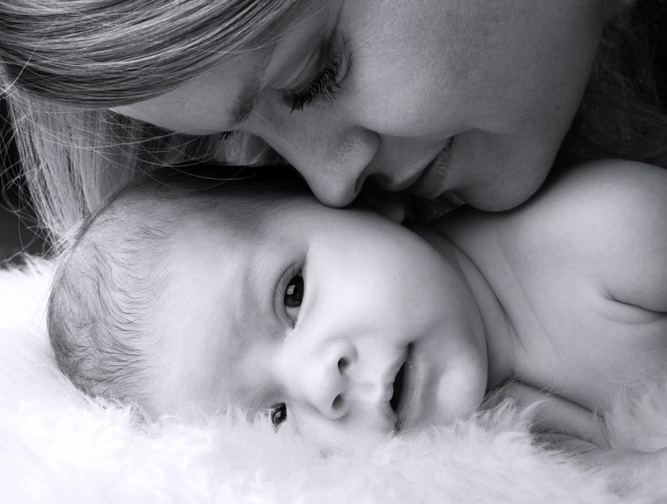 Sort/hvid babyfotografering af en mor, der ømt kysser sin baby på panden. Nærkontakt og kærlighed.