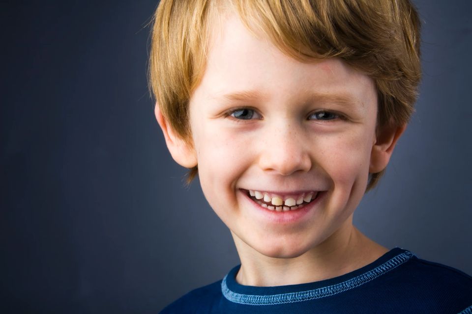 Nærbillede af en glad dreng med blondt hår, der smiler bredt mod beskueren i et naturligt og varmt børnefoto.