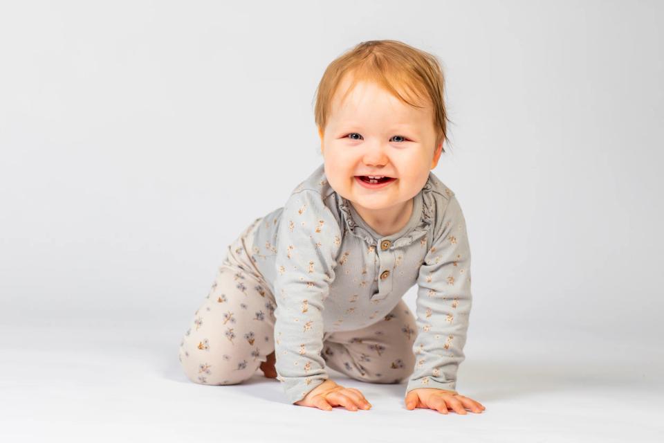 Glad baby i mønstret tøj kravler på hvid baggrund. Nyfødt fotografering med fokus på barnets smil og bevægelse.