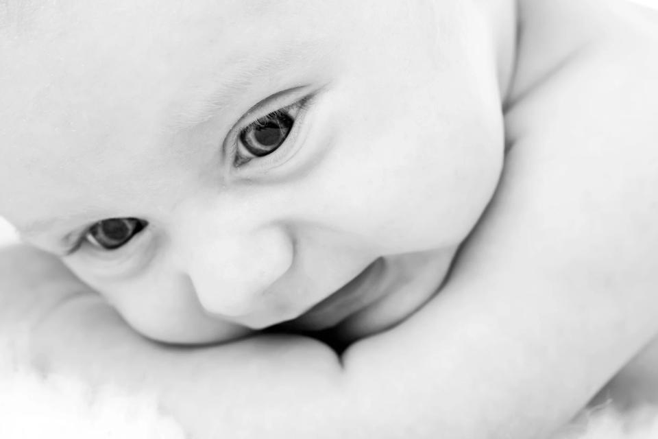 Nært babyfotografi i sort-hvid af babys øjne der kigger op, skaber en sød og nysgerrig stemning.
