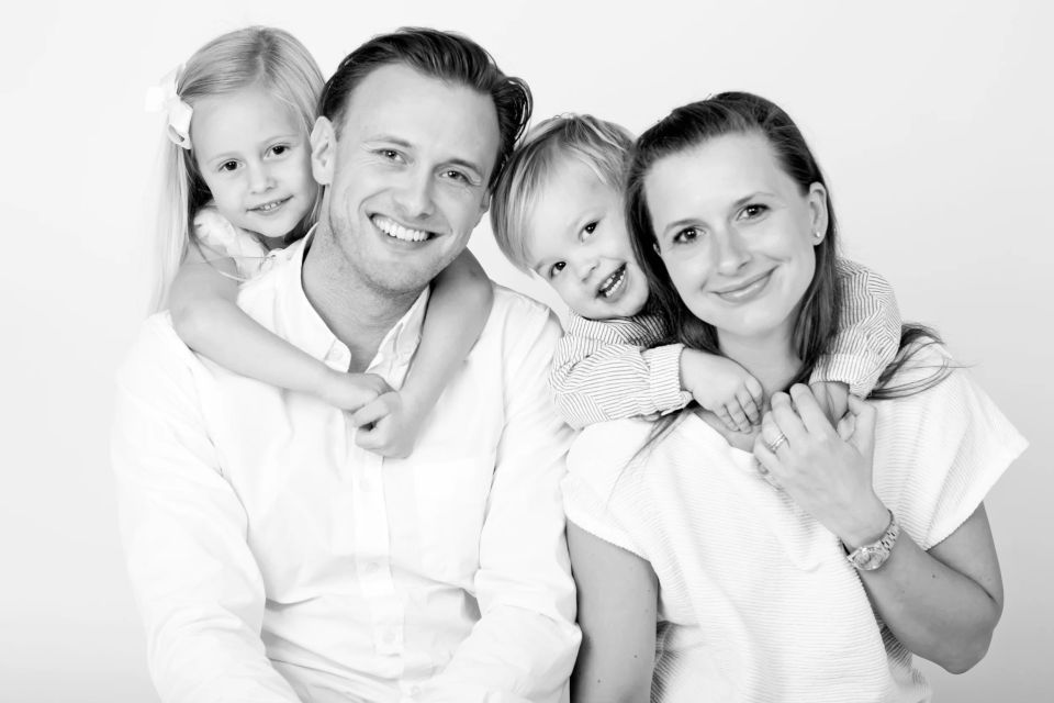 Sort-hvidt familiefoto hvor glade børn krammer deres forældre, der smiler varmt til kameraet. Et ægte børnefotografi.