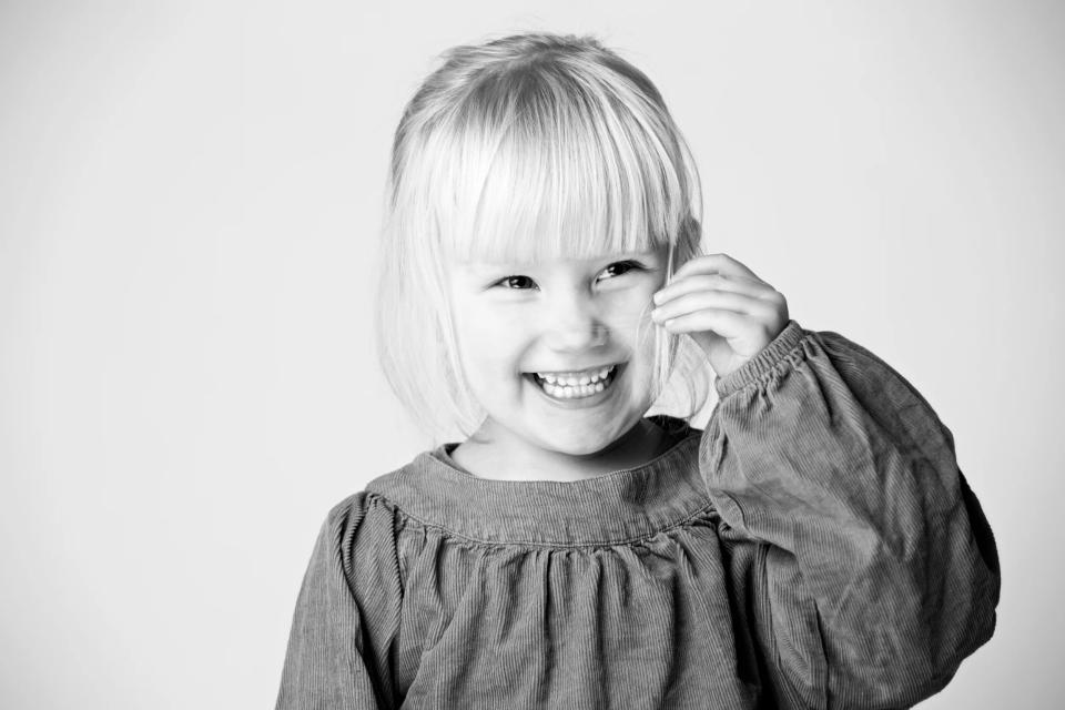 Sort-hvidt foto af et smilende barn med lyst kort hår, der griner og kigger mod beskueren. Glad og fængende børnefotografe...