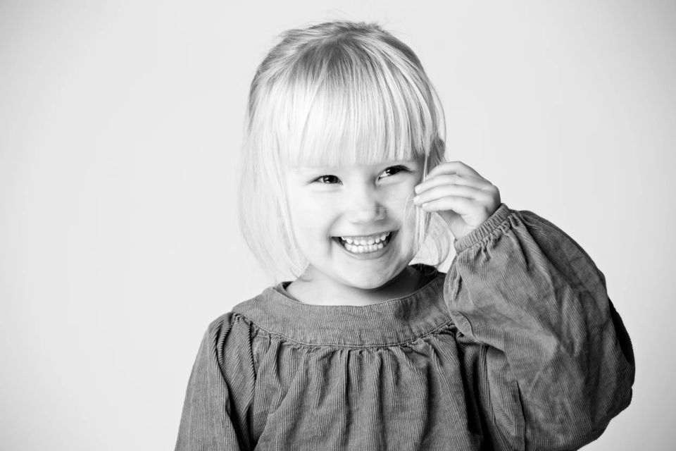 Sort-hvidt foto af et smilende barn med lyst kort hår, der griner og kigger mod beskueren. Glad og fængende børnefotografe...