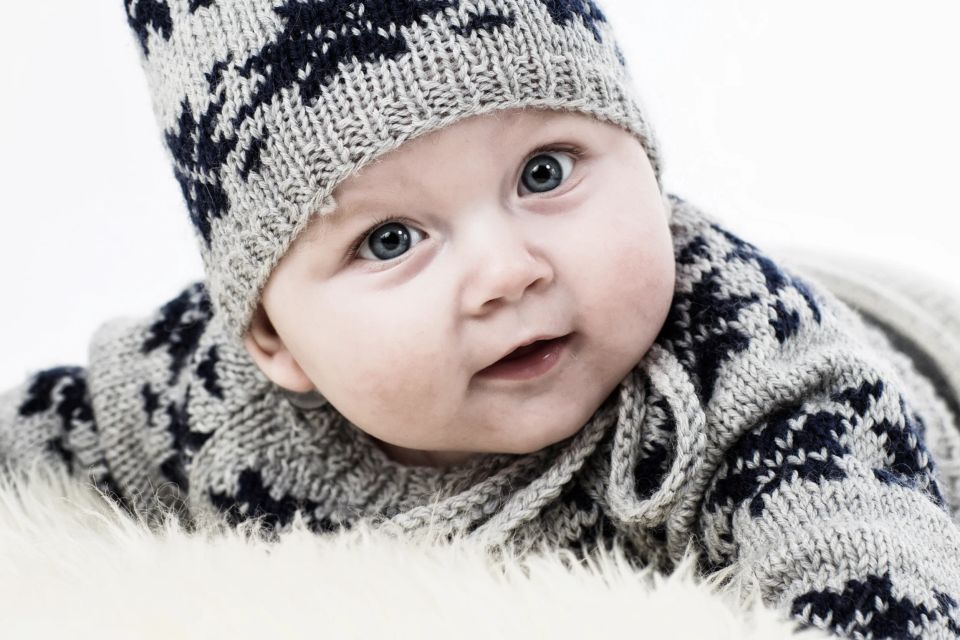 Sødt babyportræt i Virum med blå øjne i strikhue og trøje, der smiler blidt mod beskueren. Lyst, venligt lys.