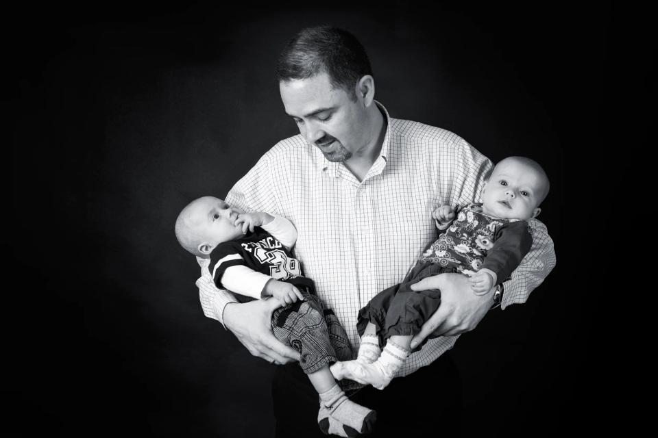 Sort-hvid familiefoto af far der kigger kærligt på tvillinger. Et autentisk portræt med fokus på relationen.