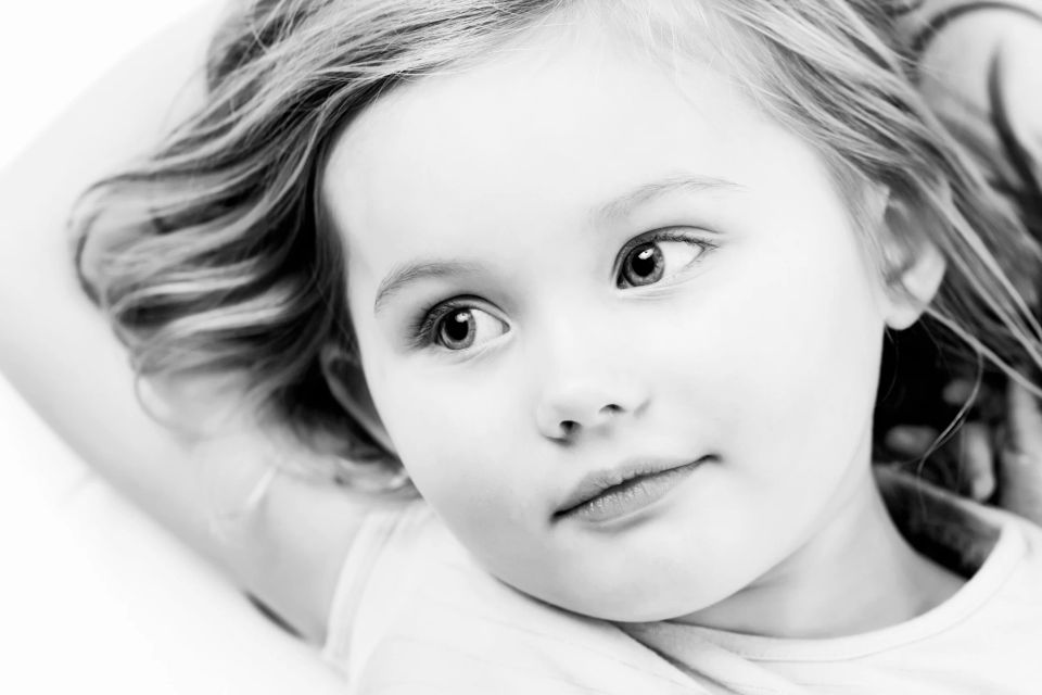 Nærbillede af et nysgerrigt barn med lyst hår, der kigger opmærksomt, i et sort/hvidt børnefotografi.