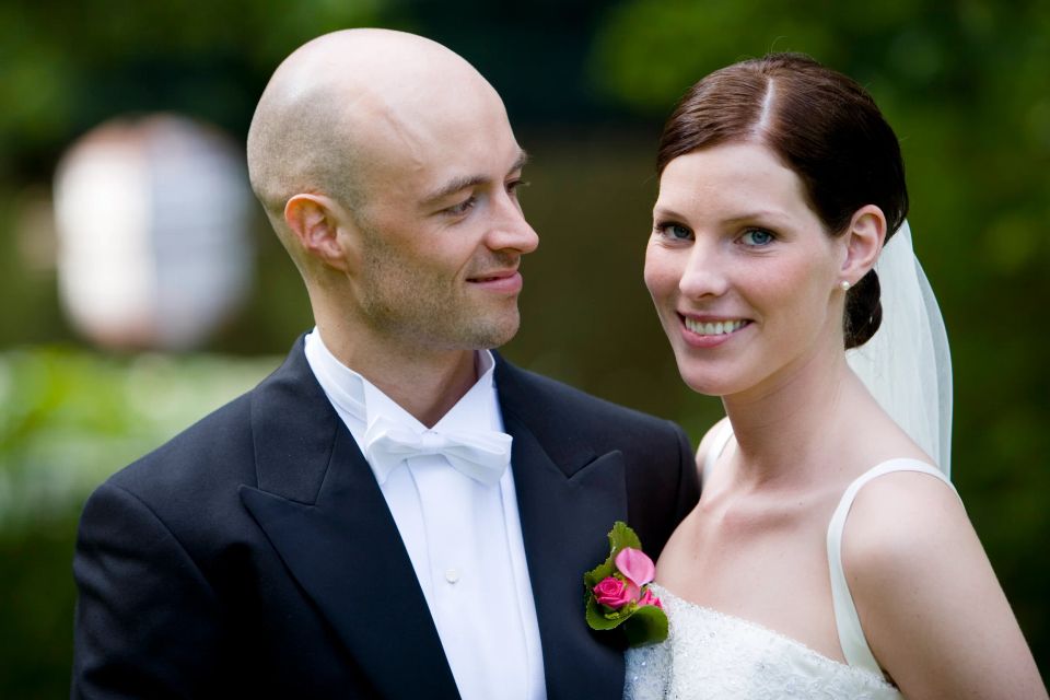 Bryllupsfoto: Smilende brudepar i nærkontakt med manden i jakkesæt med blomst og kvinden i hvid kjole i fokus