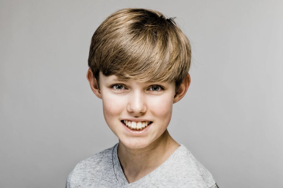 Nærbillede af glad dreng med lyst hår og autentisk smil i et lyst, klart børneportræt med venlig stemning.