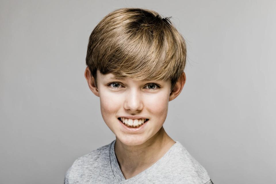 Nærbillede af glad dreng med lyst hår og autentisk smil i et lyst, klart børneportræt med venlig stemning.
