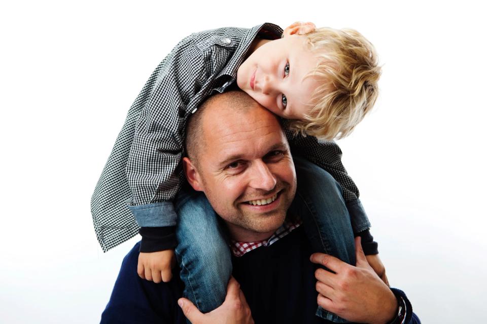 Familiefoto af smilende far med søn på skuldrene; et hjertevarmt øjeblik i studie med hvid baggrund.