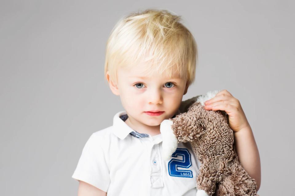 Børnefoto af nysgerrigt lille barn med blondt hår og bamse i favnen, badet i varmt lys, studiofotografering.