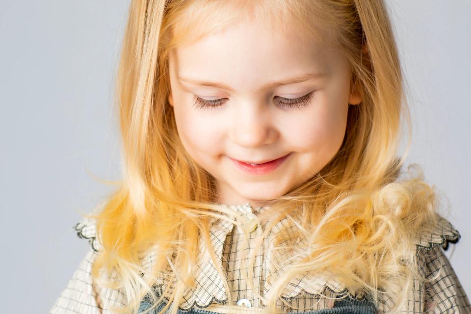 Nærbillede af et lysthåret barn med nedadvendte øjne og et svagt smil, i et ægte og kærligt familiefoto.