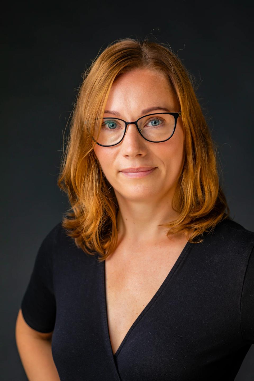 Professionelt portrætfoto af rødhåret kvinde med briller, der ser direkte ind i kameraet med et venligt udtryk.
