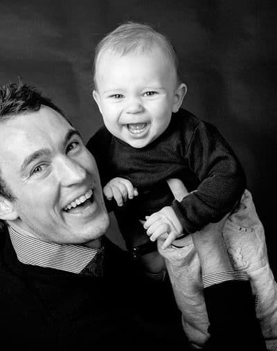 Sort-hvidt portrætbillede af en glad far og hans grinende baby, der deler et varmt øjeblik sammen.