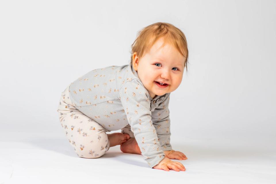 Glad baby kravler i lyseblomstret tøj mod hvid baggrund i et charmerende babyfotografi.
