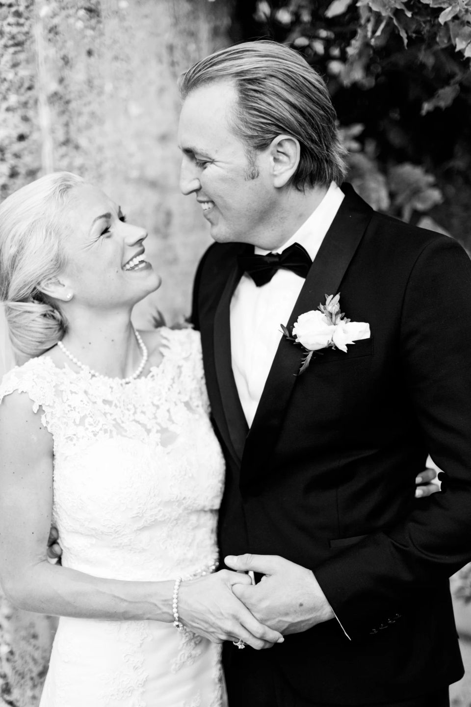 Sort/hvidt bryllupsfotografi af smilende brudepar der holder i hånd i autentisk stemning, med fokus på glæde.