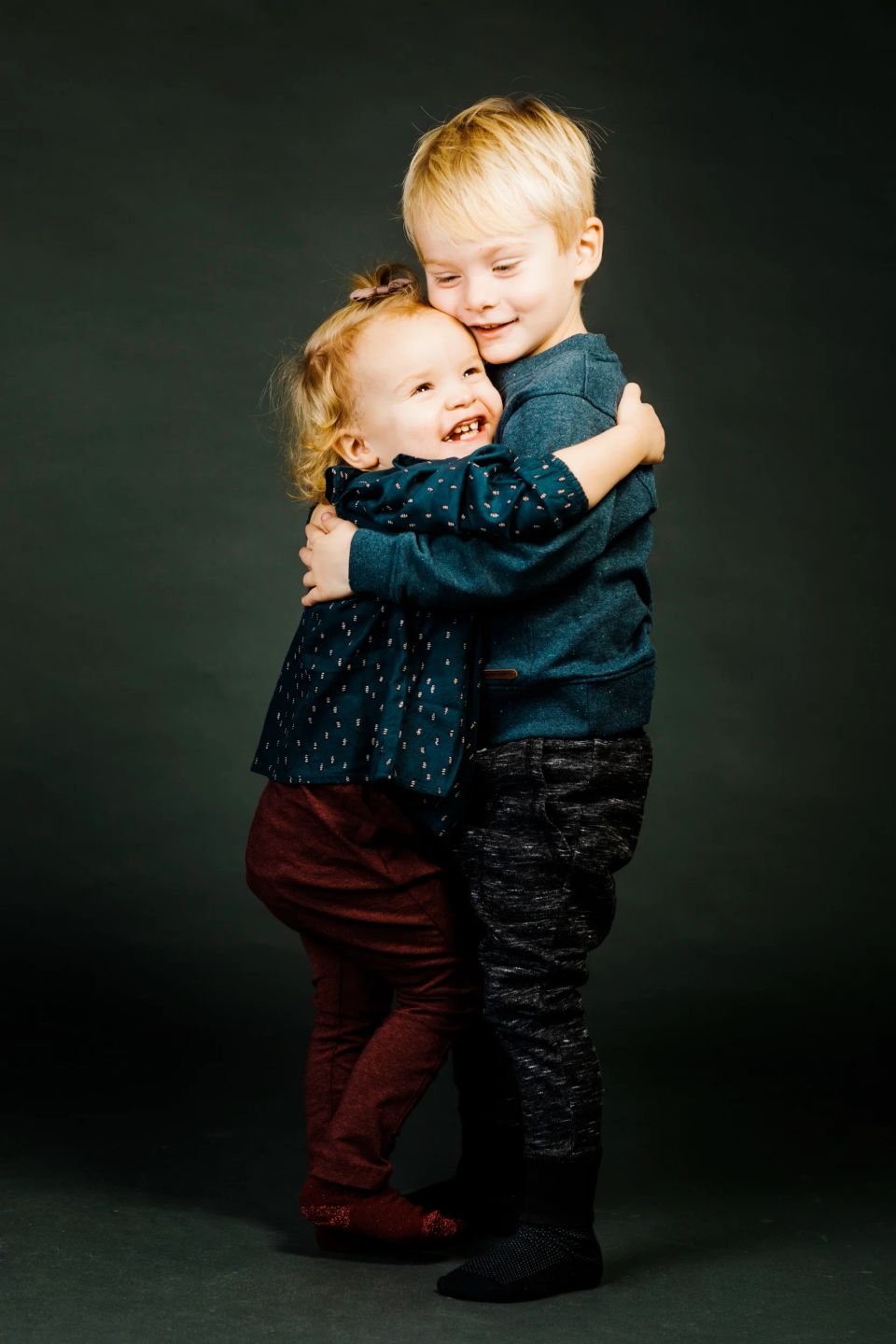 Børn: En glad lille dreng og pige i en kærlig krammer mod en mørk baggrund, med et smil der stråler. Et skønt børnefoto.