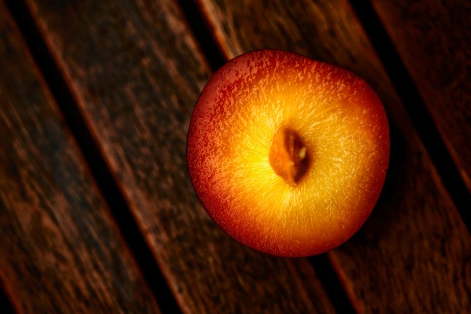 Nærbillede af en moden blomme i varmt, naturligt lys på en mørk træoverflade. Stemningsfuldt billede i kategorien andet.