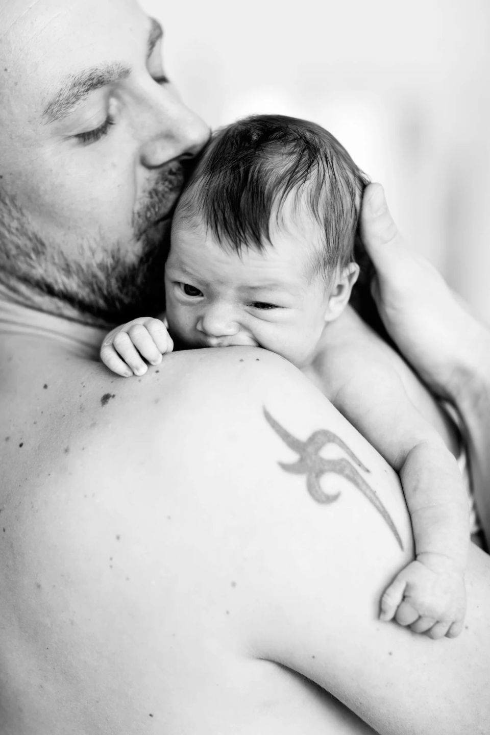 Sort/hvid nyfødt fotografering hvor en baby ligger trygt på sin fars skulder, med fars kind mod barnets hoved.