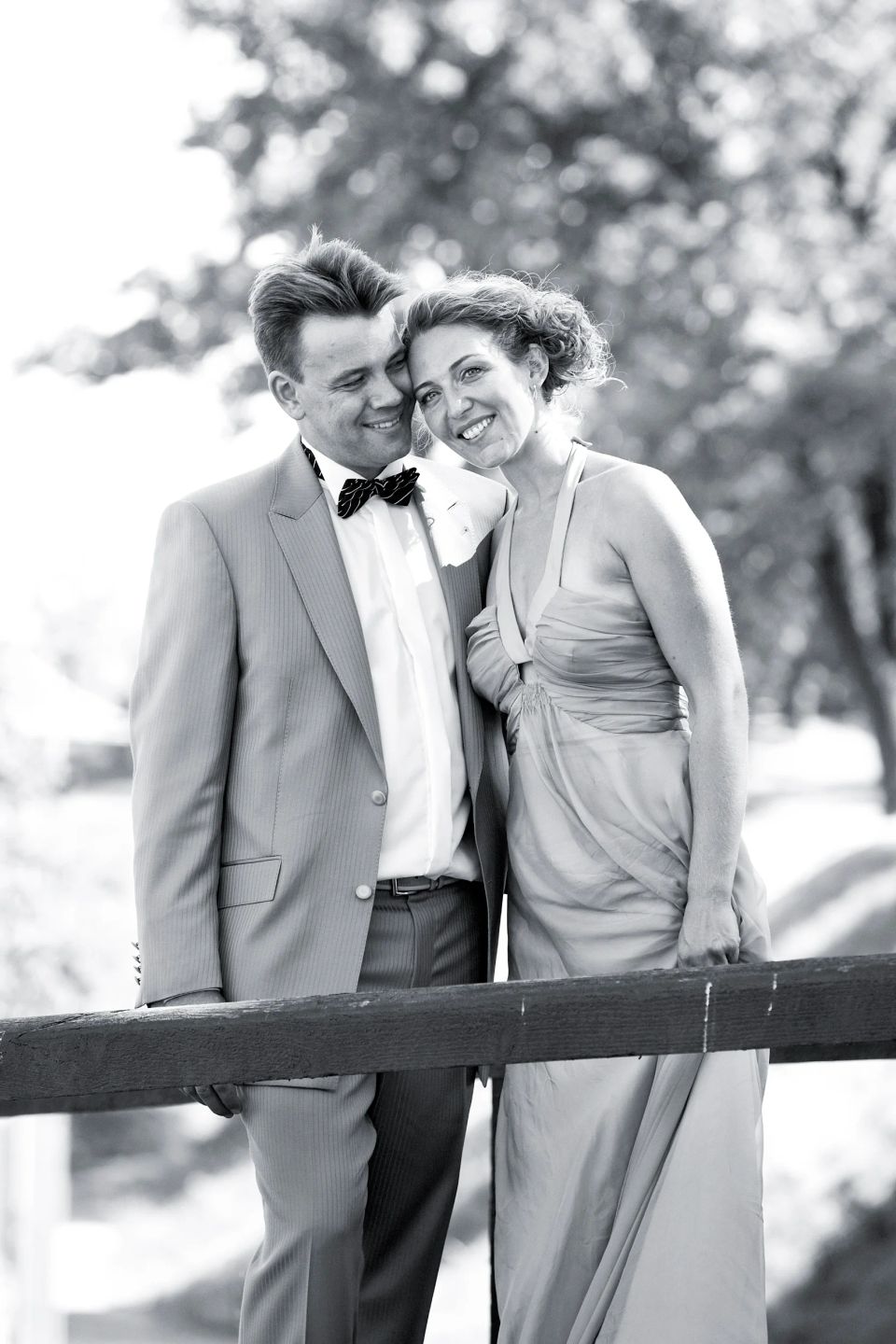 Sort/hvidt bryllupsfoto af smilende brudepar tæt sammen, med bruden der hviler hovedet mod gommens skulder.