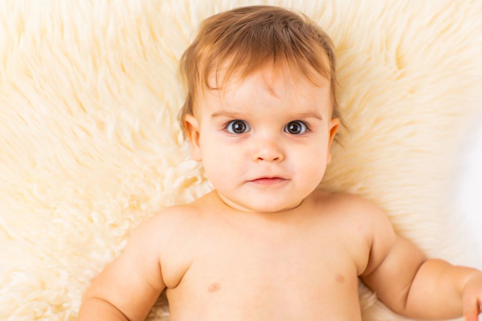 Nærbillede af baby liggende på blødt, hvidt fåreskind. Virums babyfotografering med store brune øjne og nysgerrigt udtryk.