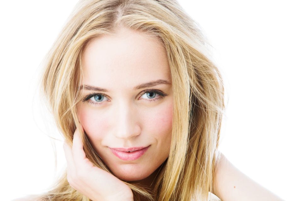 Nærbillede portrætfoto af en blond kvinde med klare blå øjne, smilende mod kameraet i blødt, lyst lys.