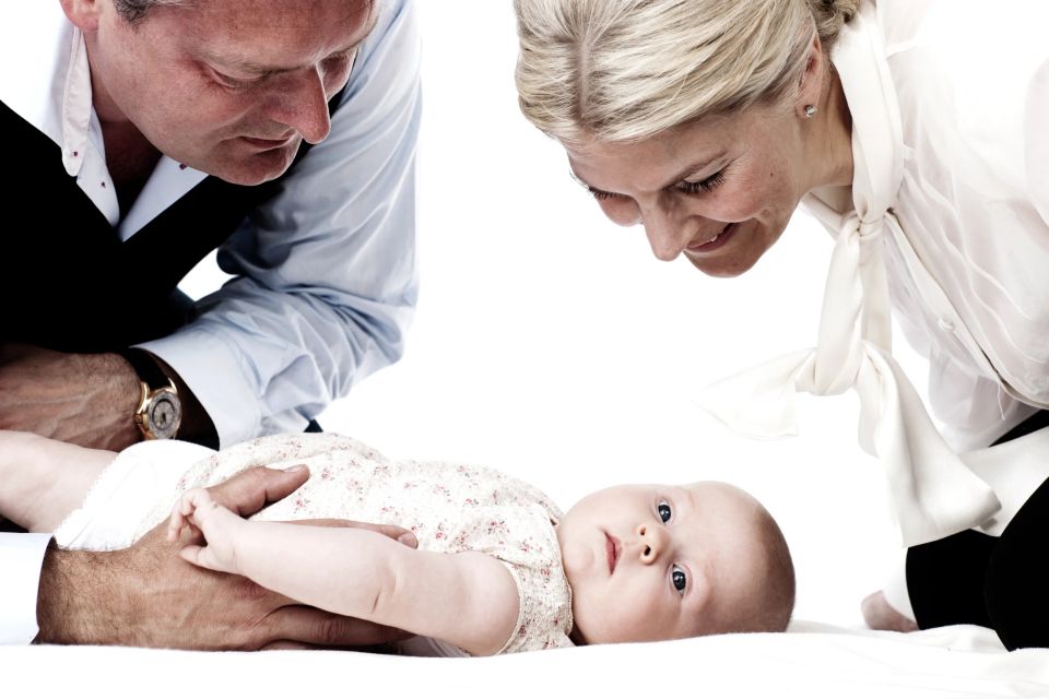 Familiefoto af forældre, der ser kærligt på deres nyfødte baby, der ligger på et hvidt tæppe. Blødt lys og lyst lys.