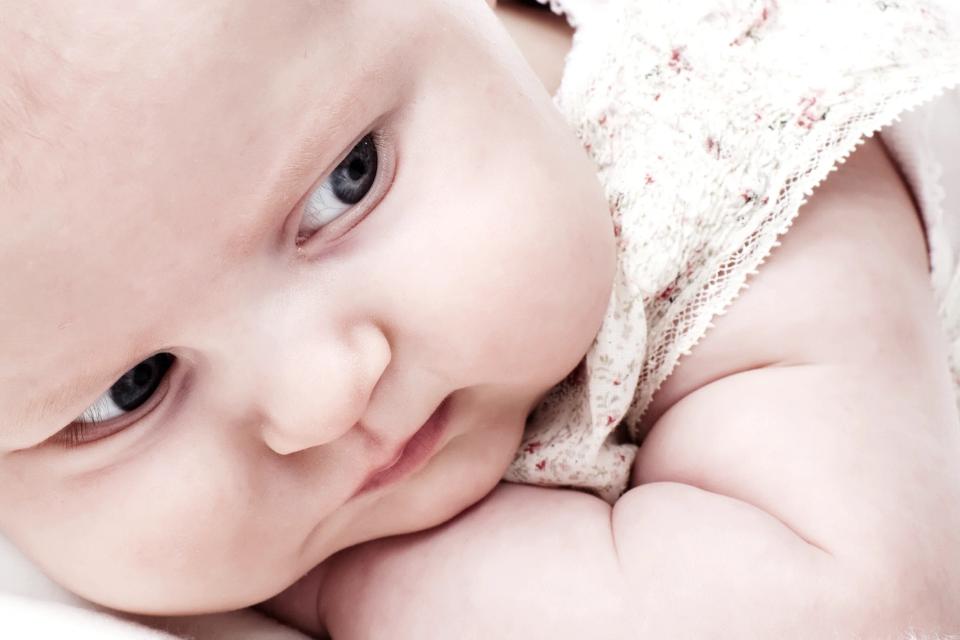 Nærbillede af baby, der kigger opmærksomt til siden med store, mørke øjne. Blød babyfotografering i naturligt lys.