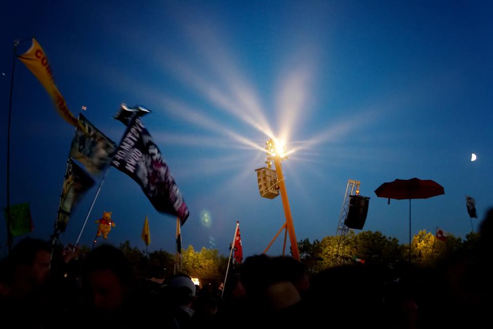Roskilde Festival om aftenen med en lysende lygtepæl og flag mod en mørkeblå himmel, skaber magisk stemning.