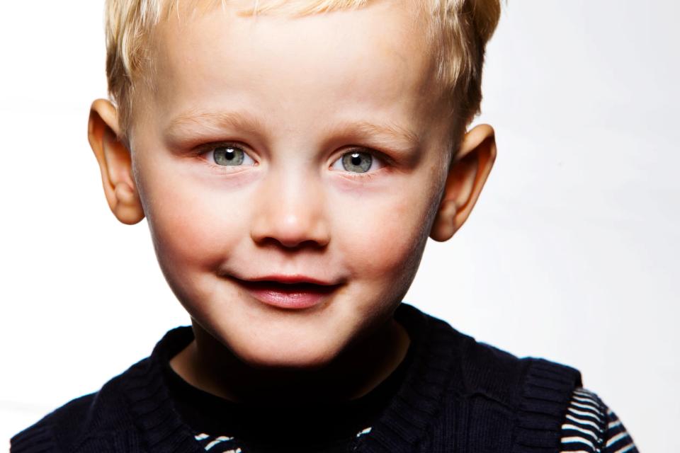 Glad blond dreng med grønne øjne smiler, tæt på kamera. Et børnefoto med fokus på ansigtets glæde.