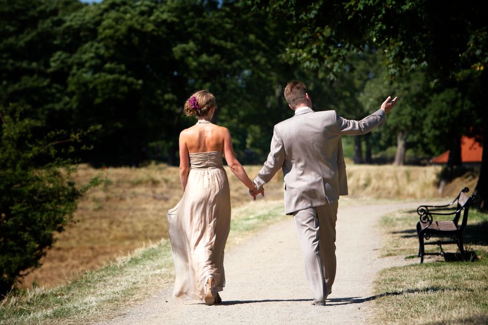 Bryllupsbillede af nygift par, der hånd i hånd går væk på en sti i sollys, mand vinker.