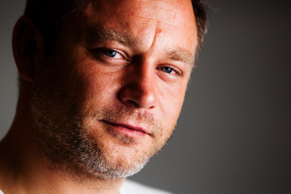 Nærbillede af mand med blå øjne og kort skæg i blød belysning, der skaber et autentisk portrætfoto.