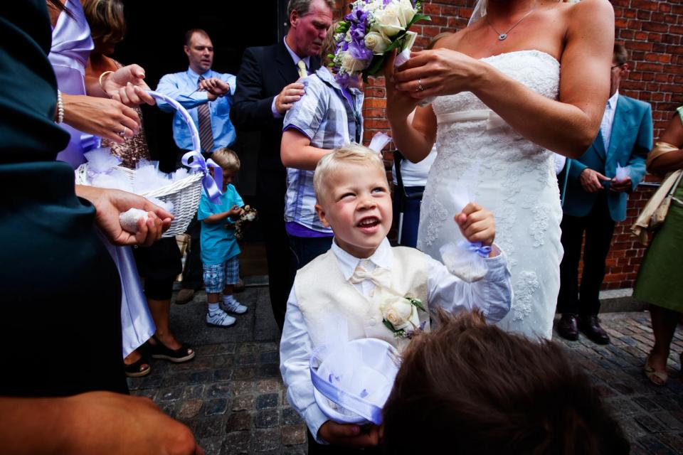 Glad lille dreng i flot vest til bryllup kigger op mod bruden med et smil, klar til at kaste ris.
