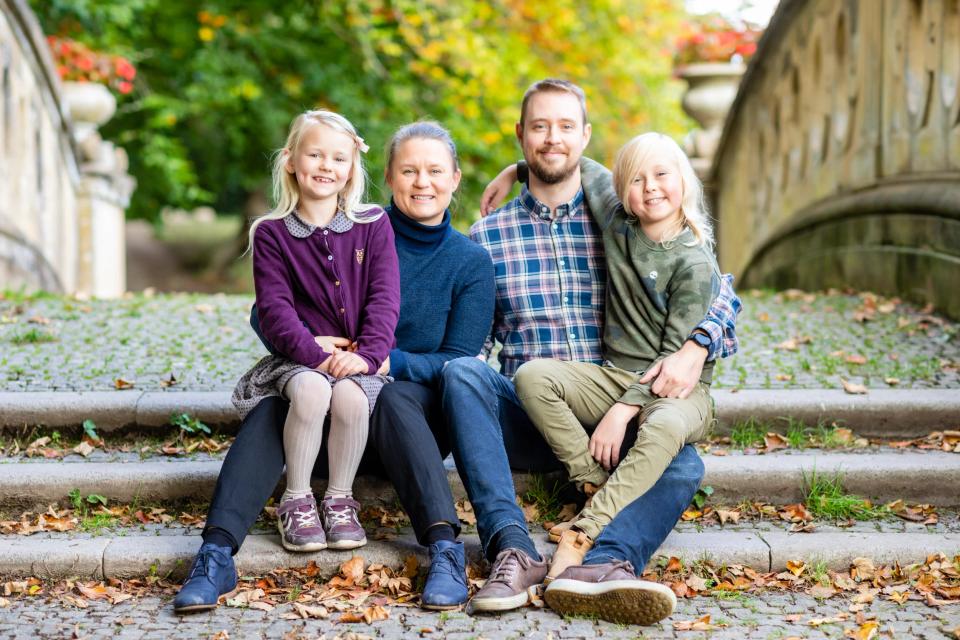 Familiefotografering i Virum: Glad familie, mor, far og to smilende børn, sidder på bro i efterårsfarver.