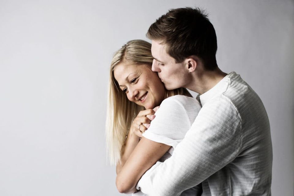 Portrætfoto af mand der kysser smilende kvinde på kinden i et ømt øjeblik, blødt lys, varm stemning.