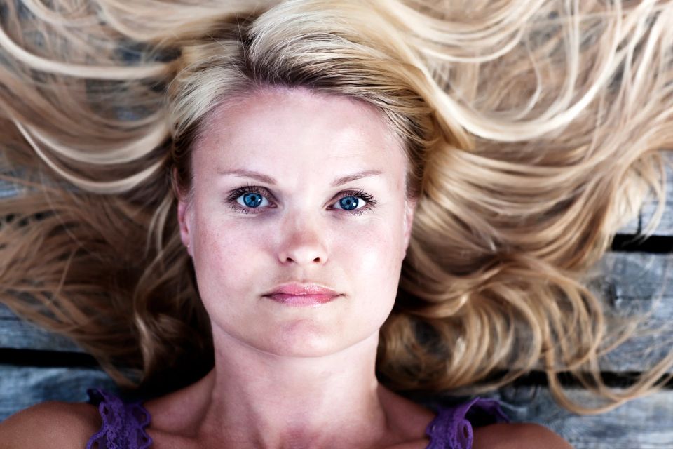 Nærbillede portræt af kvinde med blondt hår liggende på trægulv, håret spredt omkring hendes hoved, blikket er neutralt og...