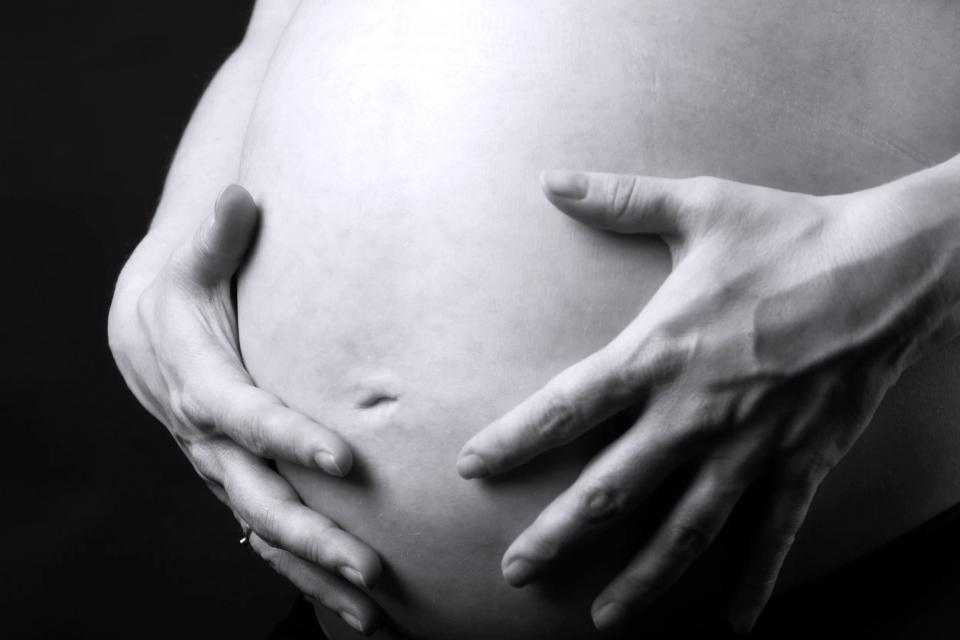 Nærbillede af gravid mave i sort/hvid, hvor hænder omfavner maven blødt, symboliserende moderskabets nærvær. Gravid fotogr...