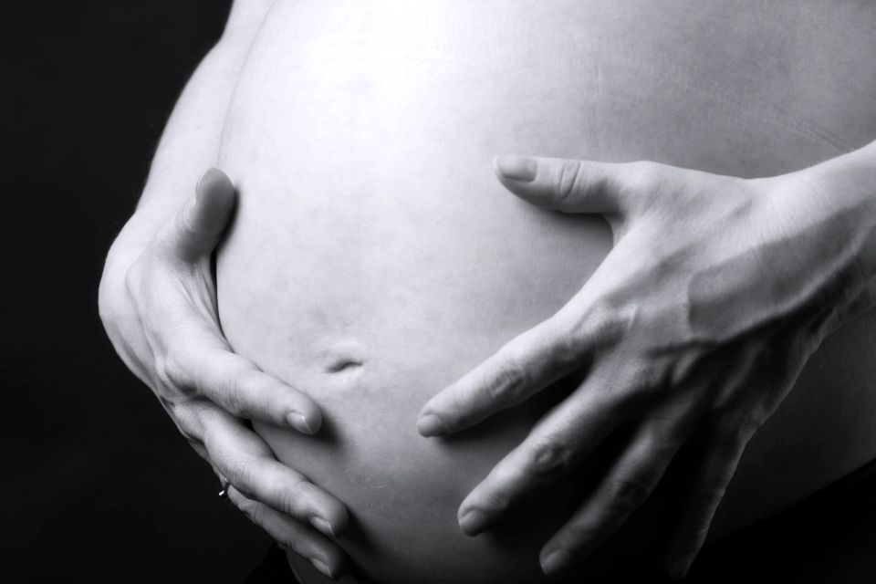 Nærbillede af gravid mave i sort/hvid, hvor hænder omfavner maven blødt, symboliserende moderskabets nærvær. Gravid fotogr...