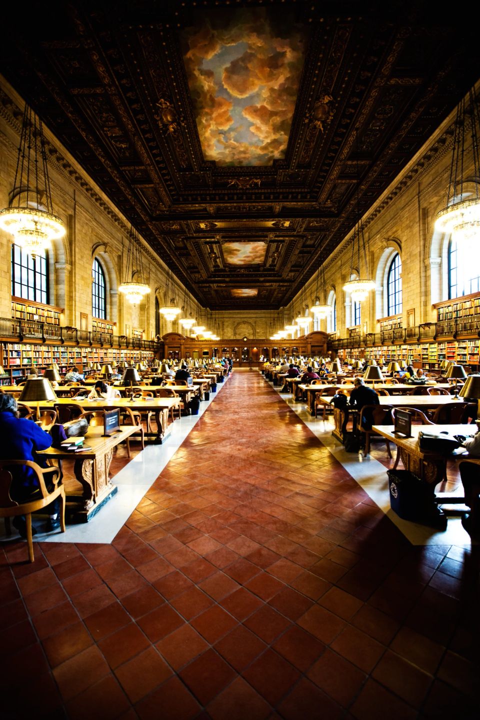 Historisk læsesal med smukt loftsmaleri i varme farver, folk studerer ved træt borde, dæmpet belysning. Stemningsfuldt foto.