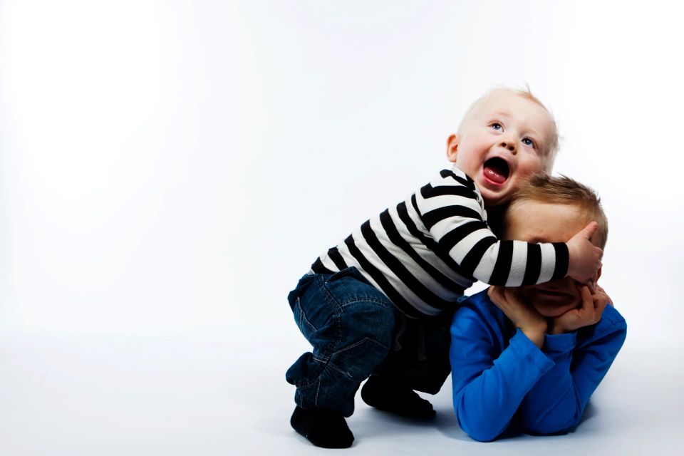 Legesyge babyer med stor mave og åben mund, den anden gemmer ansigtet, i et lyst babyfotografi.