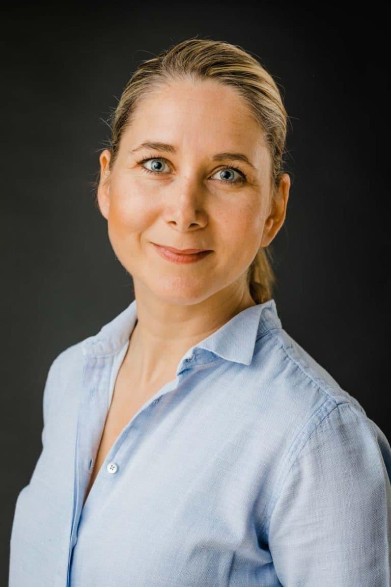 Nærbillede af kvinde med blå øjne og lyst hår i et autentisk portrætfoto med blød belysning mod mørk baggrund.