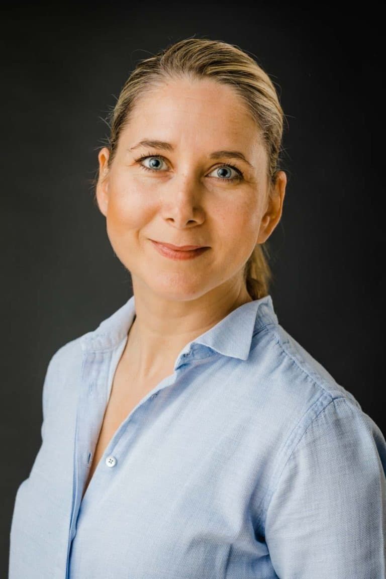 Nærbillede af kvinde med blå øjne og lyst hår i et autentisk portrætfoto med blød belysning mod mørk baggrund.