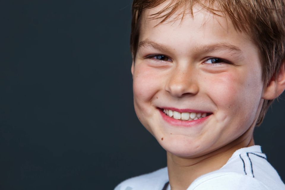 Nærbillede af glad dreng med et stort naturligt smil, fotograferet mod mørk baggrund. Et livligt børnebillede.