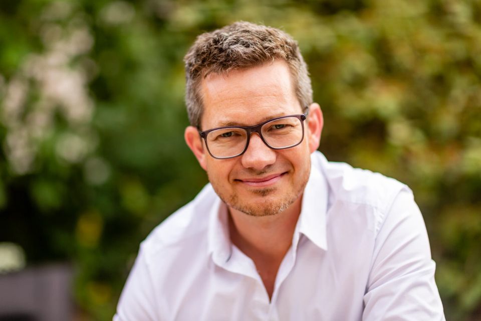 Glad mand med briller og hvid skjorte i Virum fotografering. Naturligt lys med grøn baggrund og et afslappet smil.