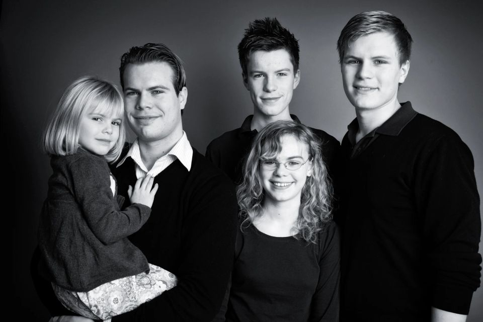 Familiebillede i sort-hvid af fem smilende søskende i forskellig alder, en ung mand holder en lille pige i armene.