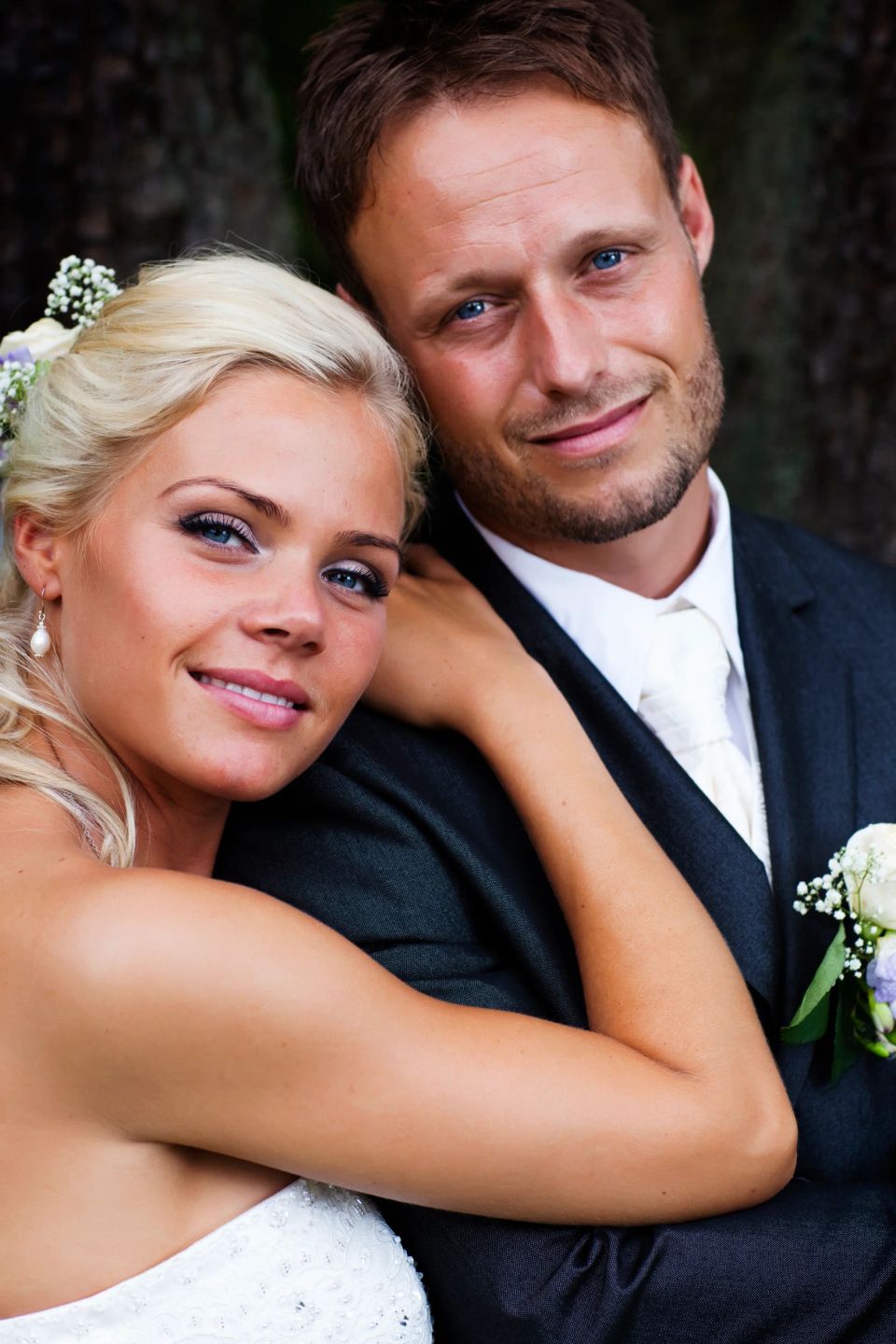 Bryllupsfotografering af smilende brud og gom tæt sammen, med blåt øjne og naturlig belysning i et nært portræt.